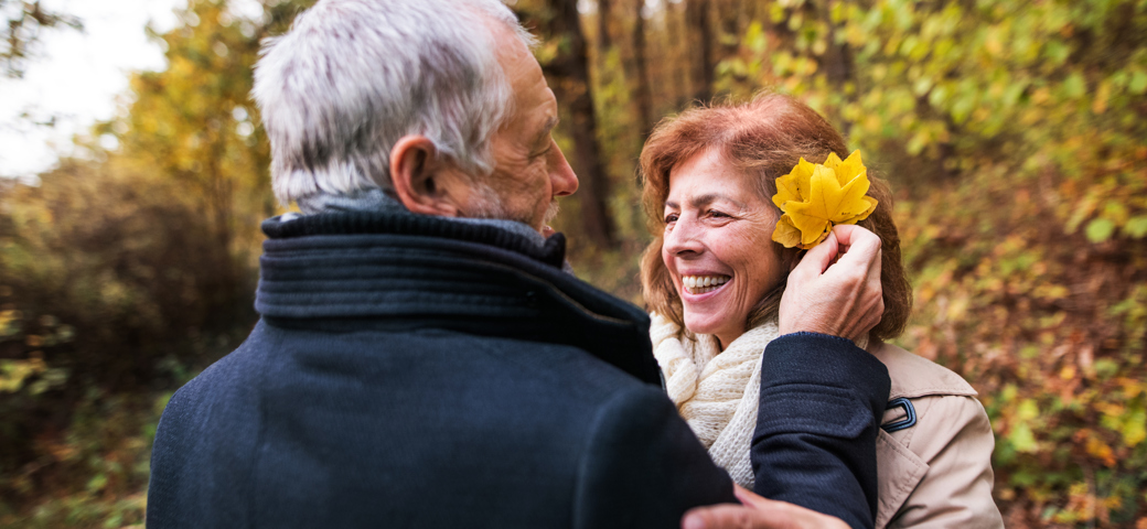 mand sætter blomst i håret på en kvinde der holder om hans arm, mens hun smiler