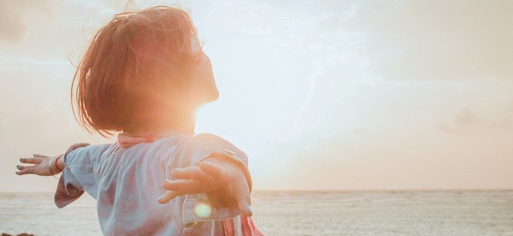 Kvinde stående med armene ud til siden ved stranden i solopgang