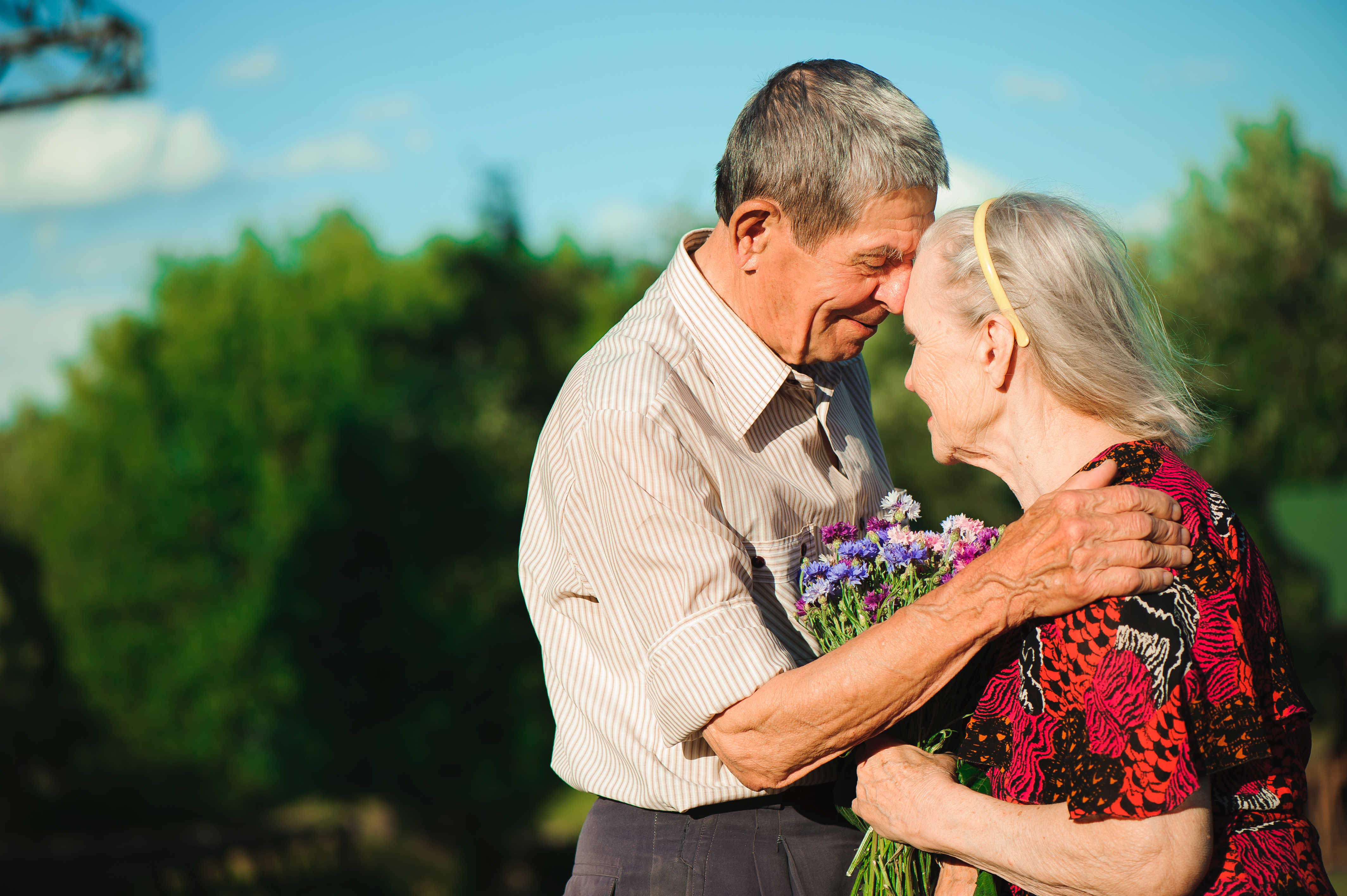 Senior mand og kvinde står holder om hinanden, mens kvinden holder blomster imellem dem