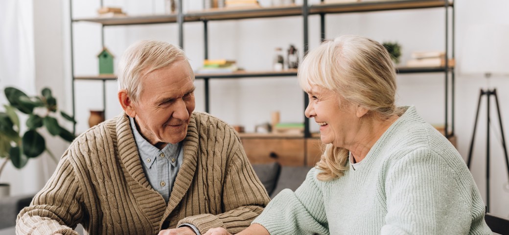 Senior par lægger puslespil ved et bord, kigger på hinanden og smiler