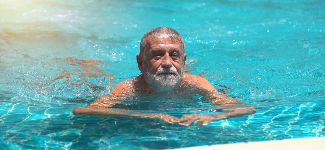 Mand svømmer i swimmingpool henimod kameraet